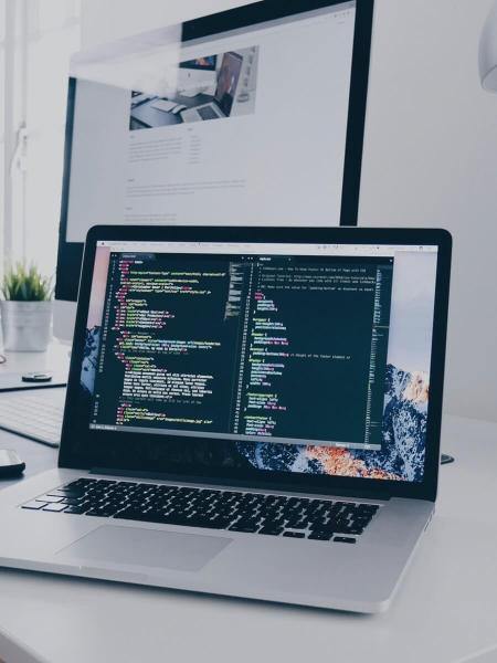 Laptop displaying code on a desk, with a monitor in the background.